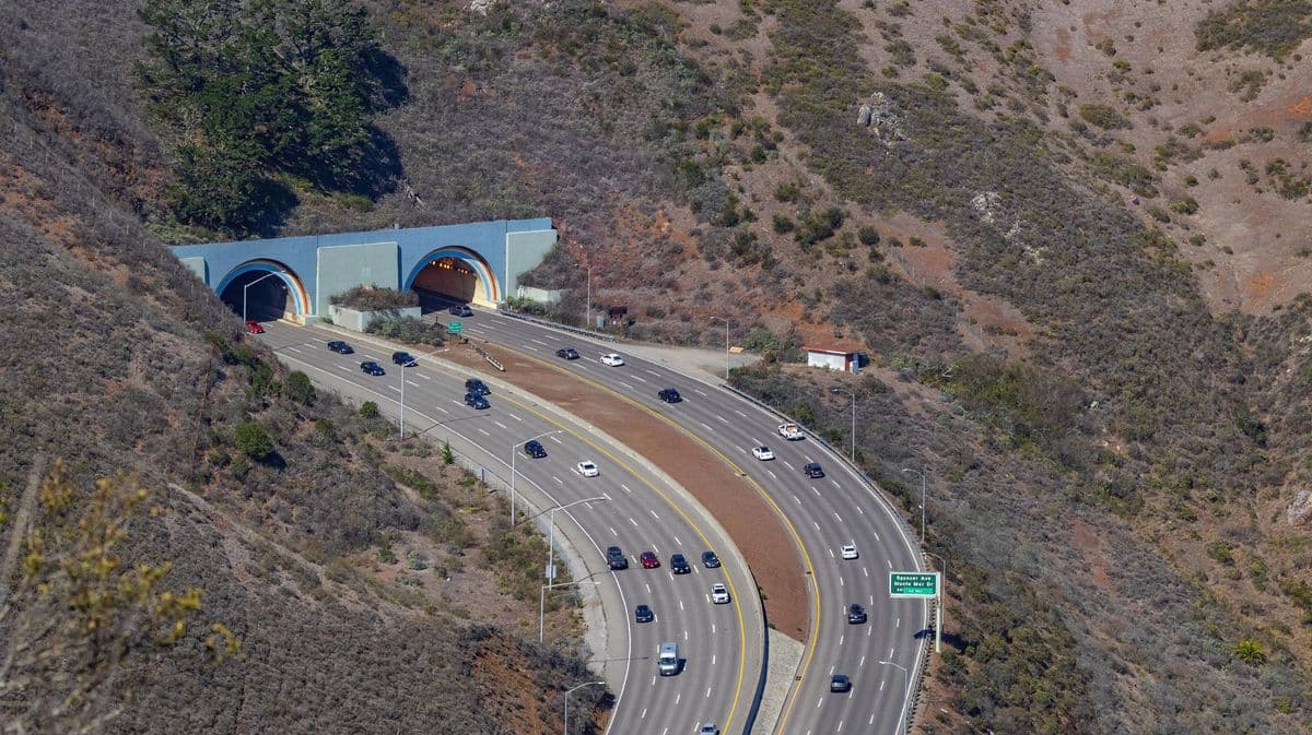 Aerial photo capturing traffic flowing through scenic highway tunnels surrounded by hills.