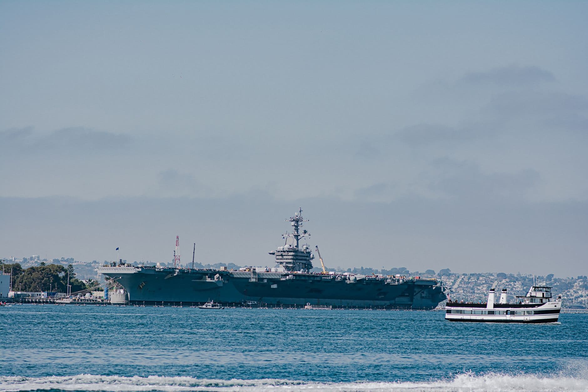 USS Carl Vinson aircraft carrier docked in San Diego harbor with a ferry in view.